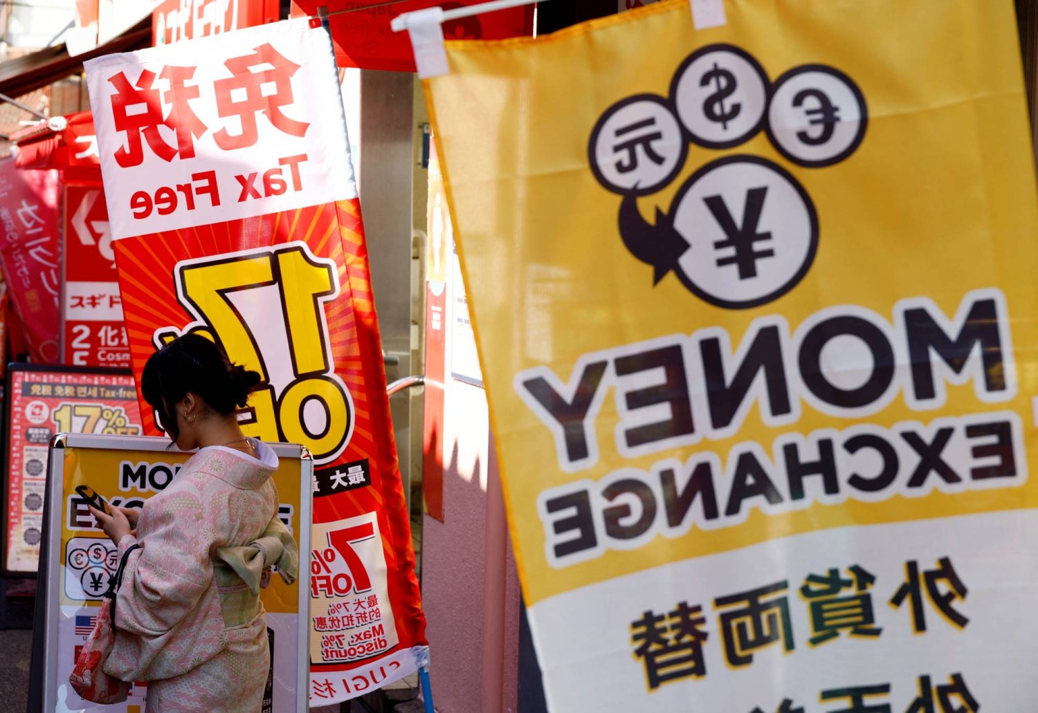 سيدة ترتدي الكيمونو الياباني أمام محل صيرفة بالعاصمة طوكيو (رويترز)