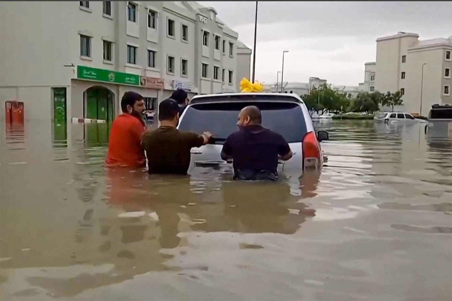 أشخاص يدفعون سيارة تقطعت بهم السبل على طول شارع غمرته المياه في دبي (أ.ف.ب)