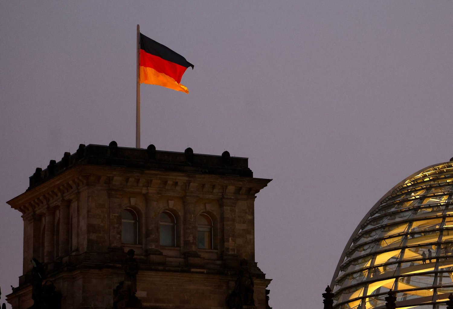 العلم الوطني الألماني يرفرف فوق مبنى الرايخستاغ المضيء مقر مجلس النواب الألماني في برلين (رويترز)