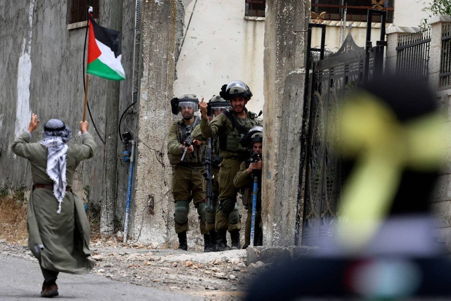 A demonstrator brandishing a Palestinian national flag walks past Israeli troops, during confrontations with them following a protest against the expropriation of Palestinian land by Israel in the occupied-West Bank, in the village of Kfar Qaddum, near the Jewish settlement of Kedumim, on June 9, 2023. (Photo by Jaafar ASHTIYEH / AFP)

